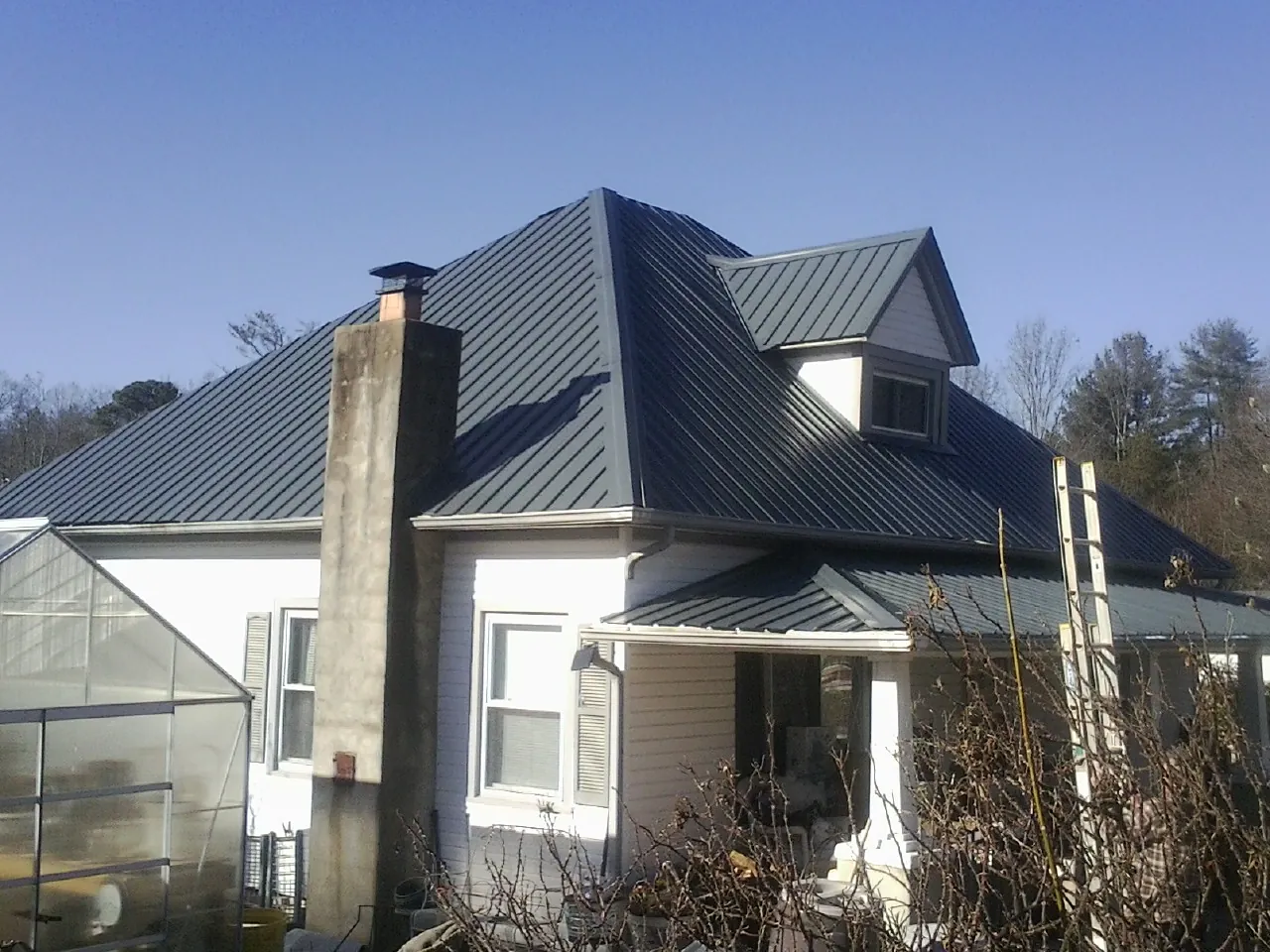 Dark blue standing seam metal roof on a white farmhouse with dormer — Slate & Tile Roof Repair by Roofing Brothers in Linthicum Heights