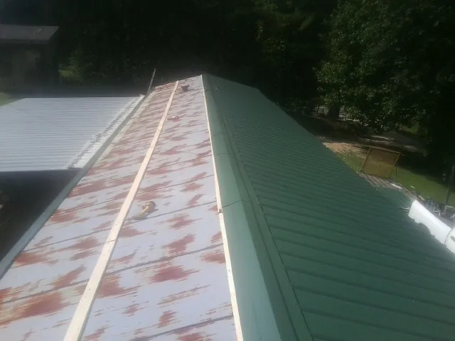 Old rusted panels beside newly installed green metal roofing — Wind Damage Roof Repair by Roofing Brothers in Linthicum Heights