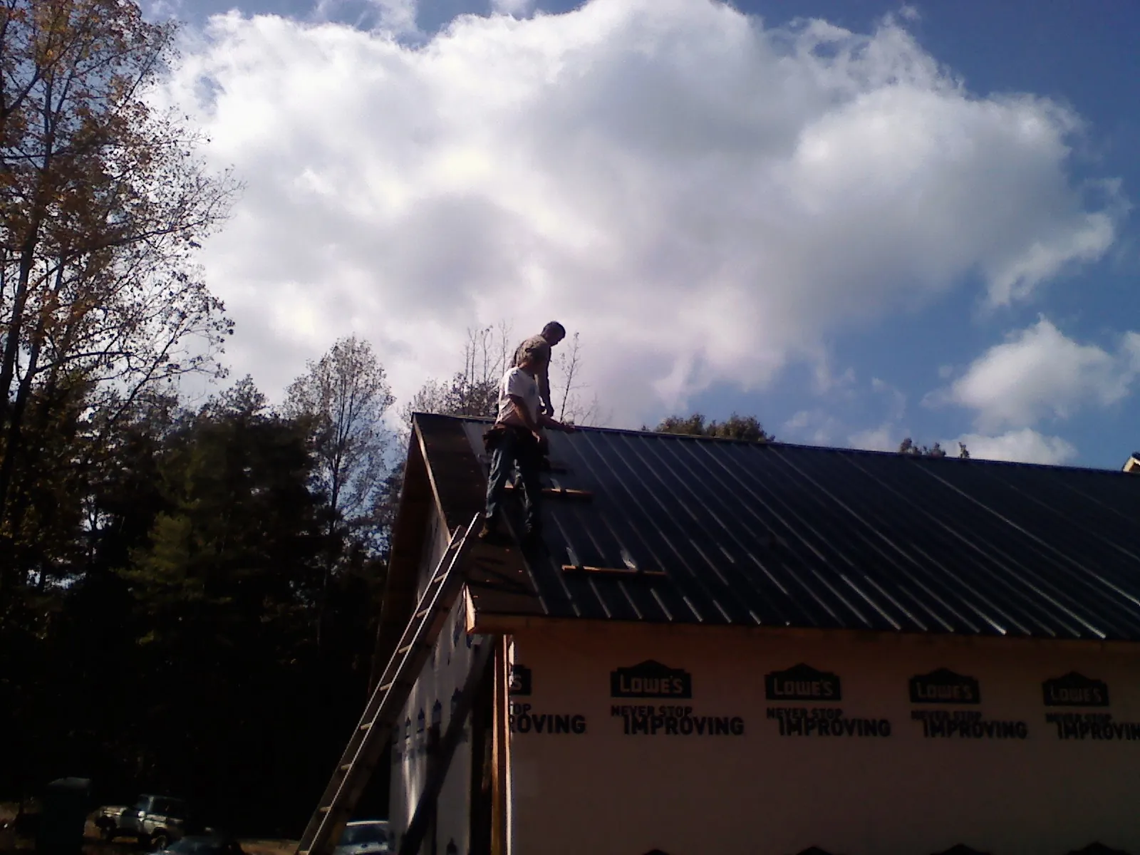 Roofer fastening dark metal panels high against a cloudy sky, from a Roof Inspection job in Linthicum Heights