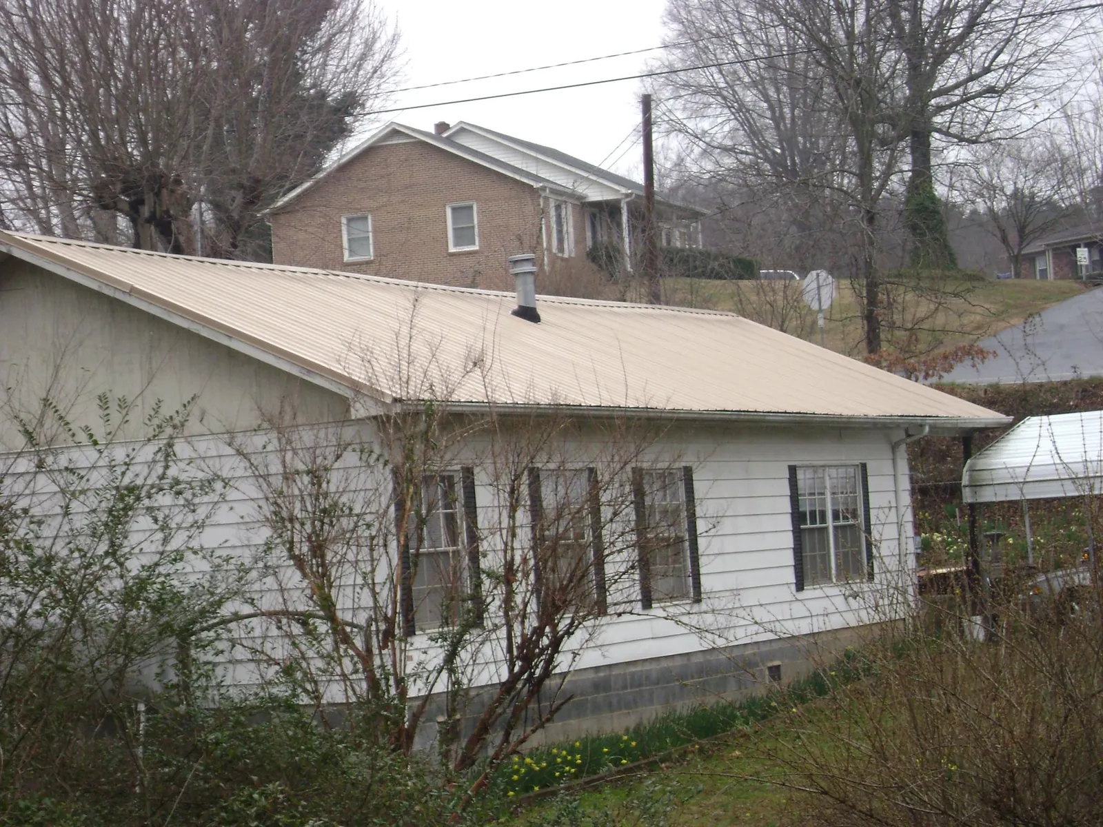 Tan metal roof on a white sided house set into a hillside — Commercial Roofing by Roofing Brothers in Linthicum Heights